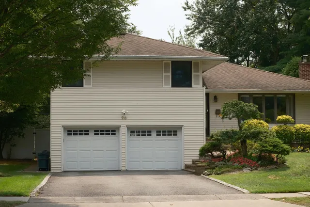 Two-story beige house with white double garage doors and a landscaped front yard